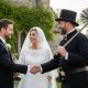 A smiling bride and groom shaking hands with a traditional chimney sweep wearing a top hat and carrying a brush, celebrating the good luck tradition of chimney sweep wedding appearances.