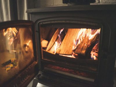 A close-up view of bright flames burning seasoned logs inside a clean black cast iron wood-burning stove with the door open, showing a well-serviced fireplace after a visit from a chimney sweep.