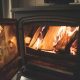 A close-up view of bright flames burning seasoned logs inside a clean black cast iron wood-burning stove with the door open, showing a well-serviced fireplace after a visit from a chimney sweep.